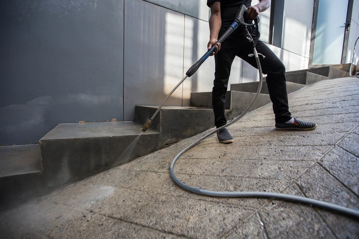 Ouvrier en tenue de travail déposant des débris dans une benne à ordures verte de grande capacité, pleine de gravats et mobilier en bois démoli