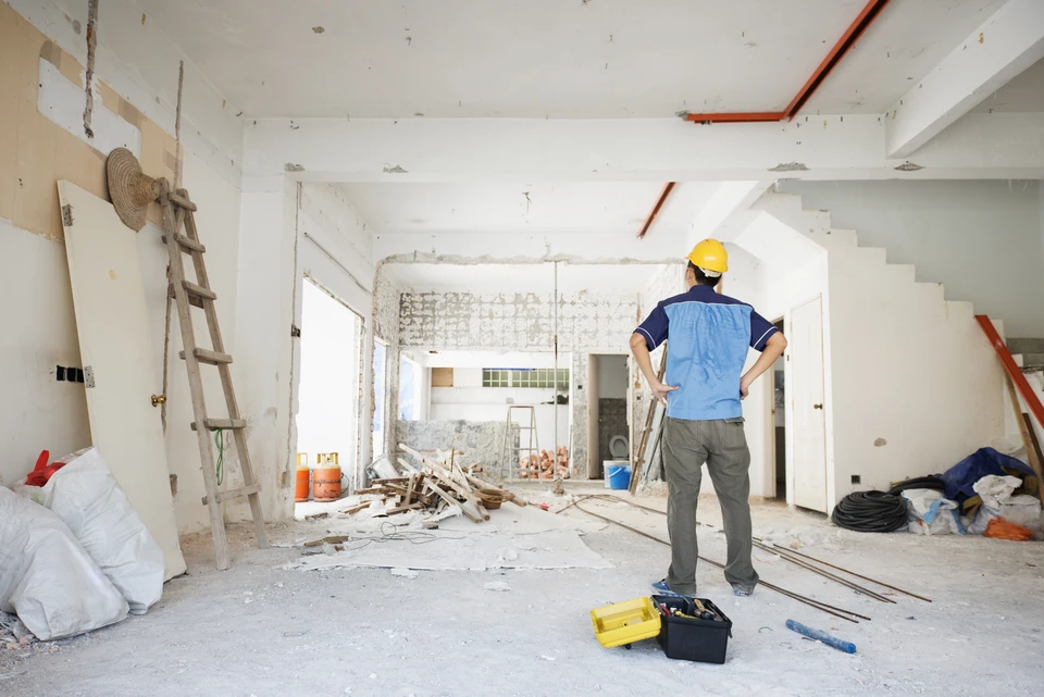 Équipe de deux ouvriers en équipement de protection (casque, gilet haute visibilité, masque) dans un appartement en cours de curage, vidant des encombrants et débris dans des bennes, démontrant le professionnalisme et la disponibilité de l'équipe Silio face au chantier